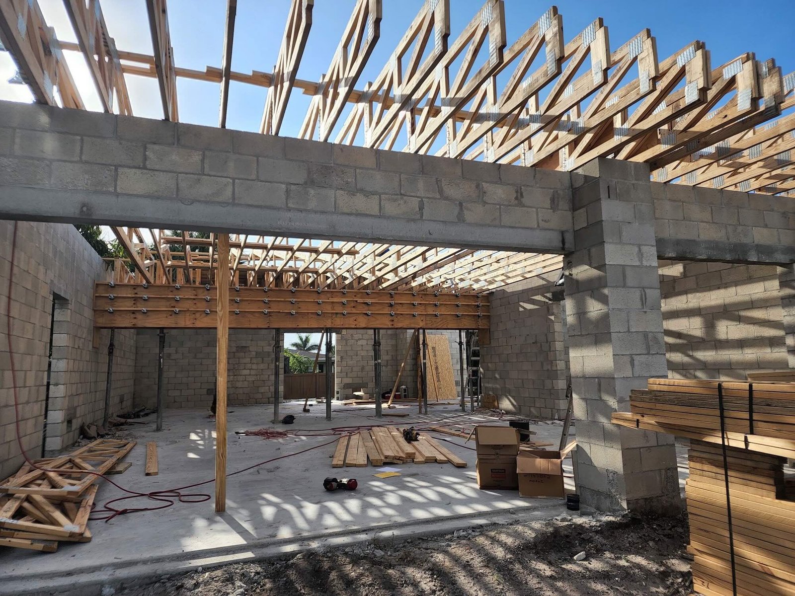 Heavy multi-ply, bolted wood beam spanning between two CMU columns, temporarily supported on adjustable steel shoring posts, with roof trusses landing on top