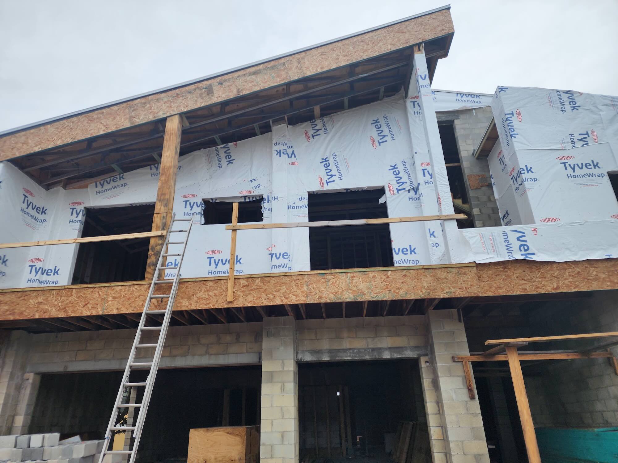 Two-story home shell wrapped in Tyvek HomeWrap, window openings cut in, ladder against the facade