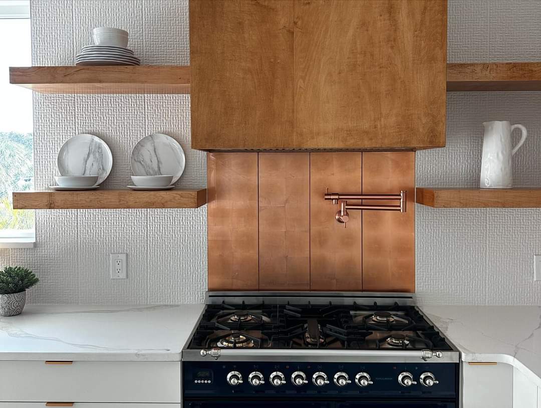 Close-up of gas range with hand-hammered copper backsplash, wood range hood, and pot filler