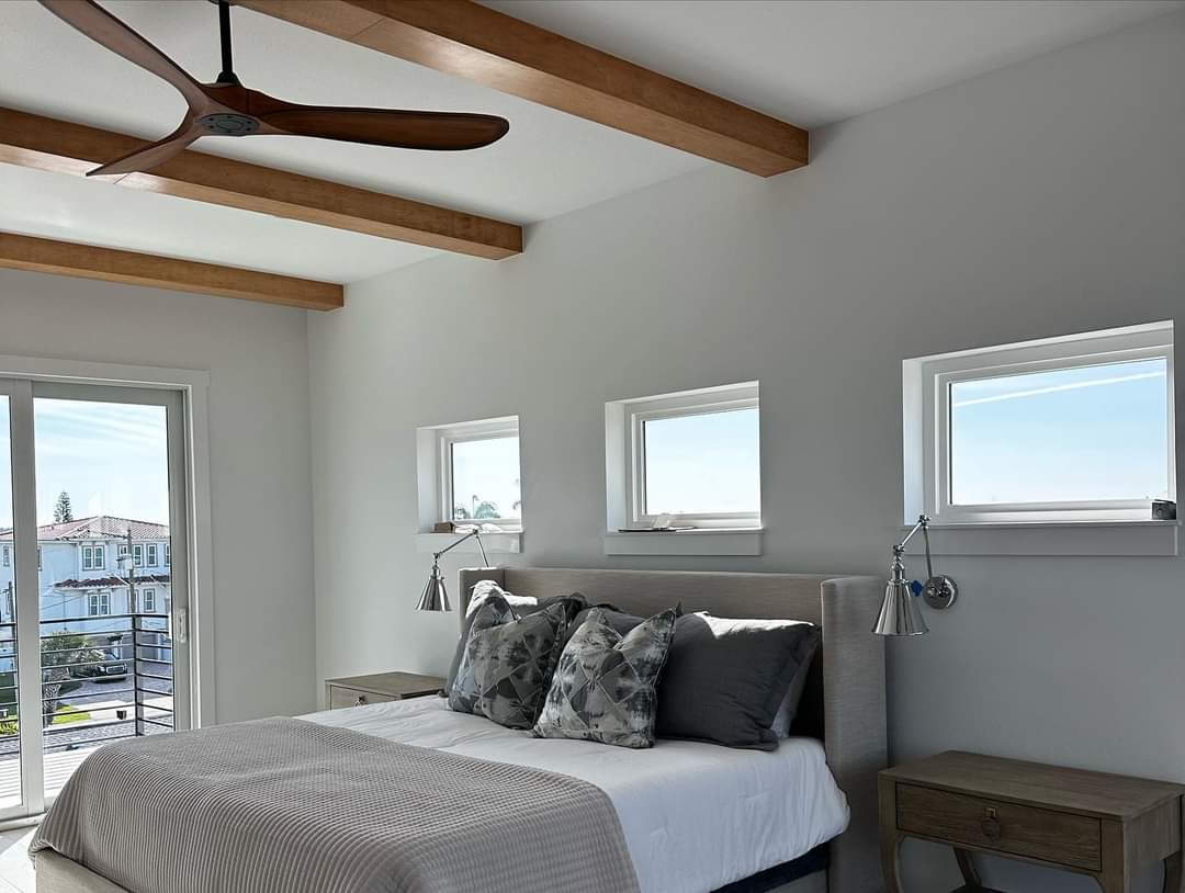 Primary bedroom with exposed timber ceiling beams, wood ceiling fan, and sliding glass door to balcony