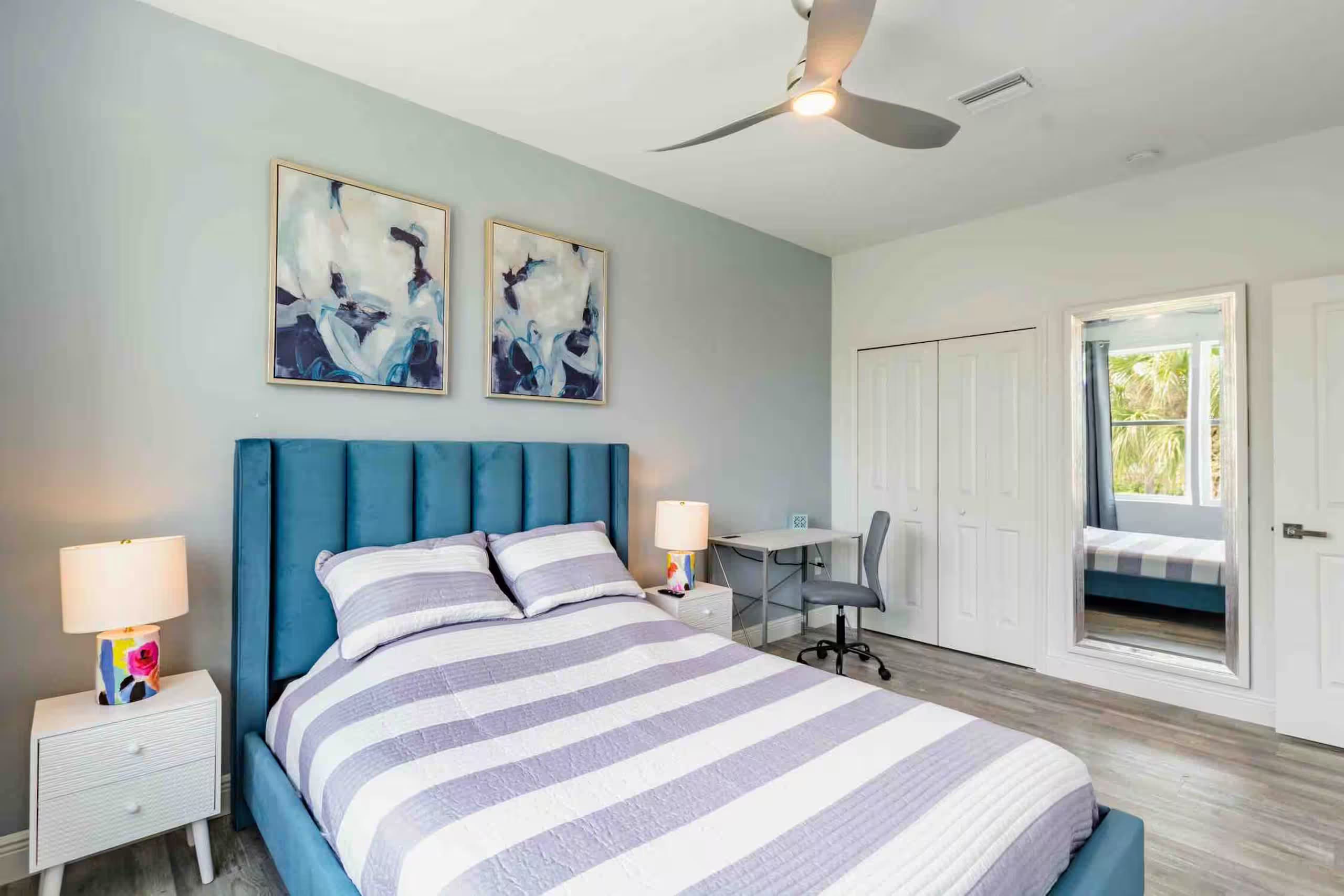 Bedroom with a teal upholstered bed, striped bedding, paired abstract art, and a built-in desk nook