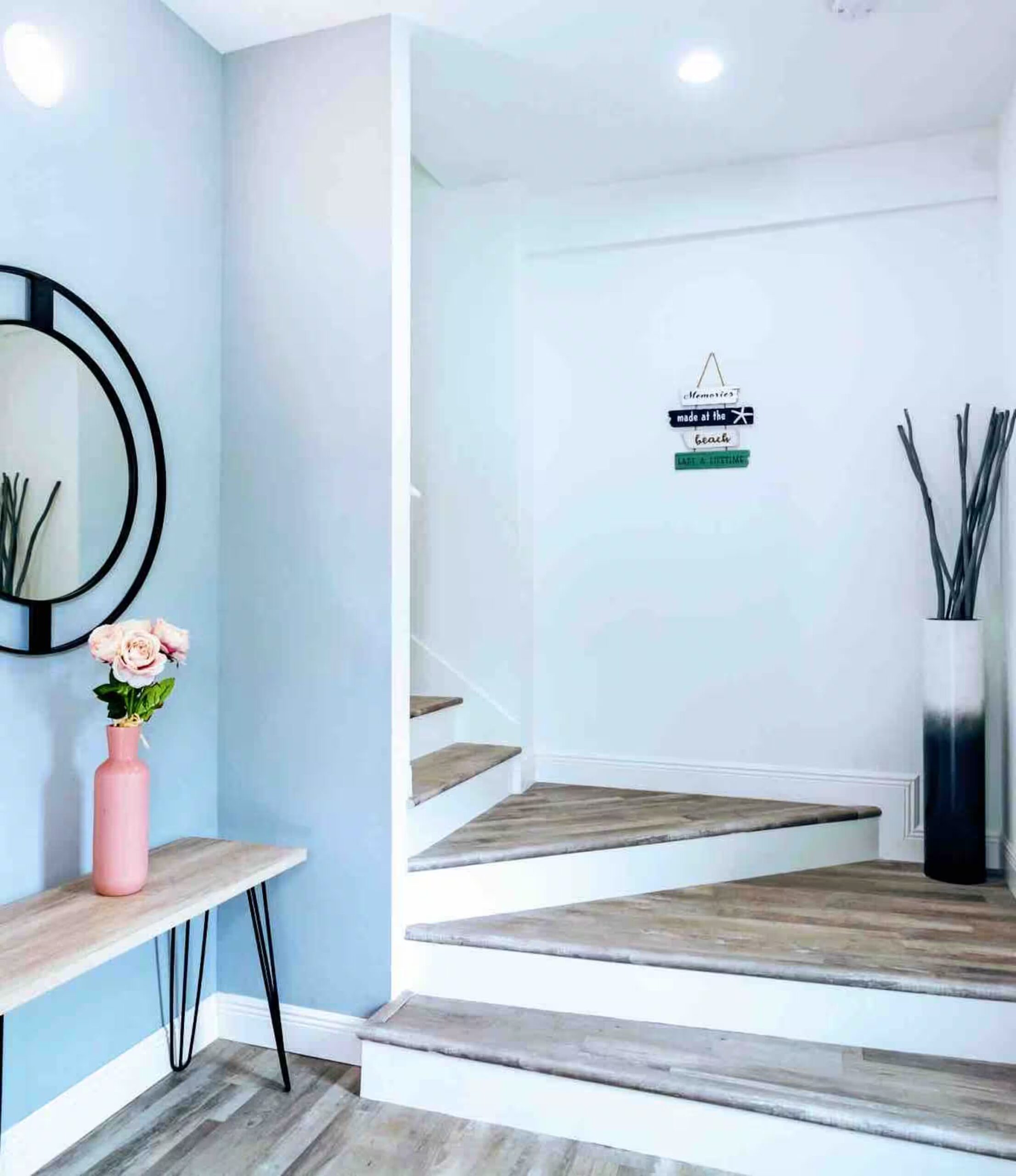 Entry hallway with a round black-framed mirror, console table, and a wood-toned open staircase