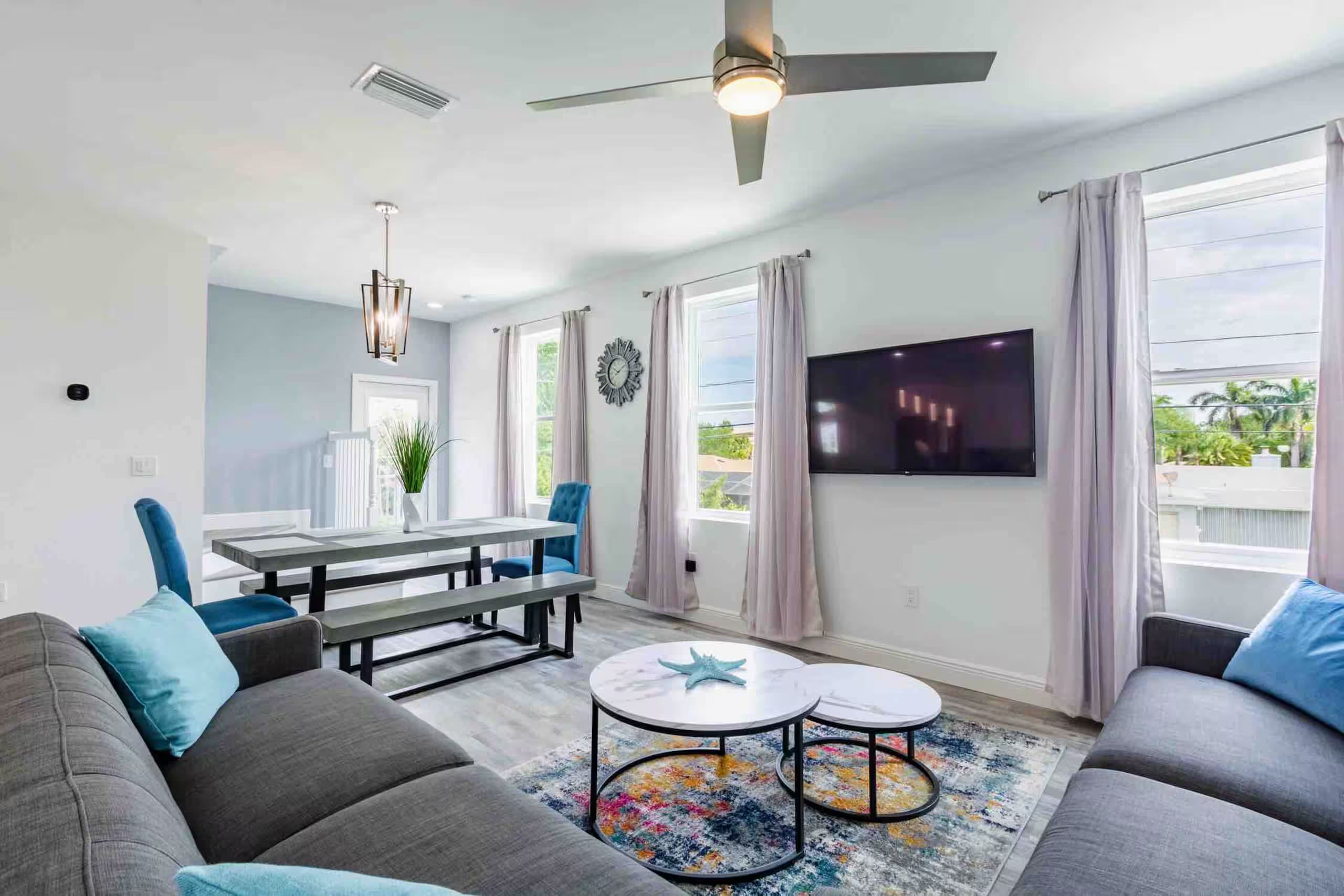 Open living room with a gray sectional sofa, blue accent pillows, and a dining table visible in the adjoining space