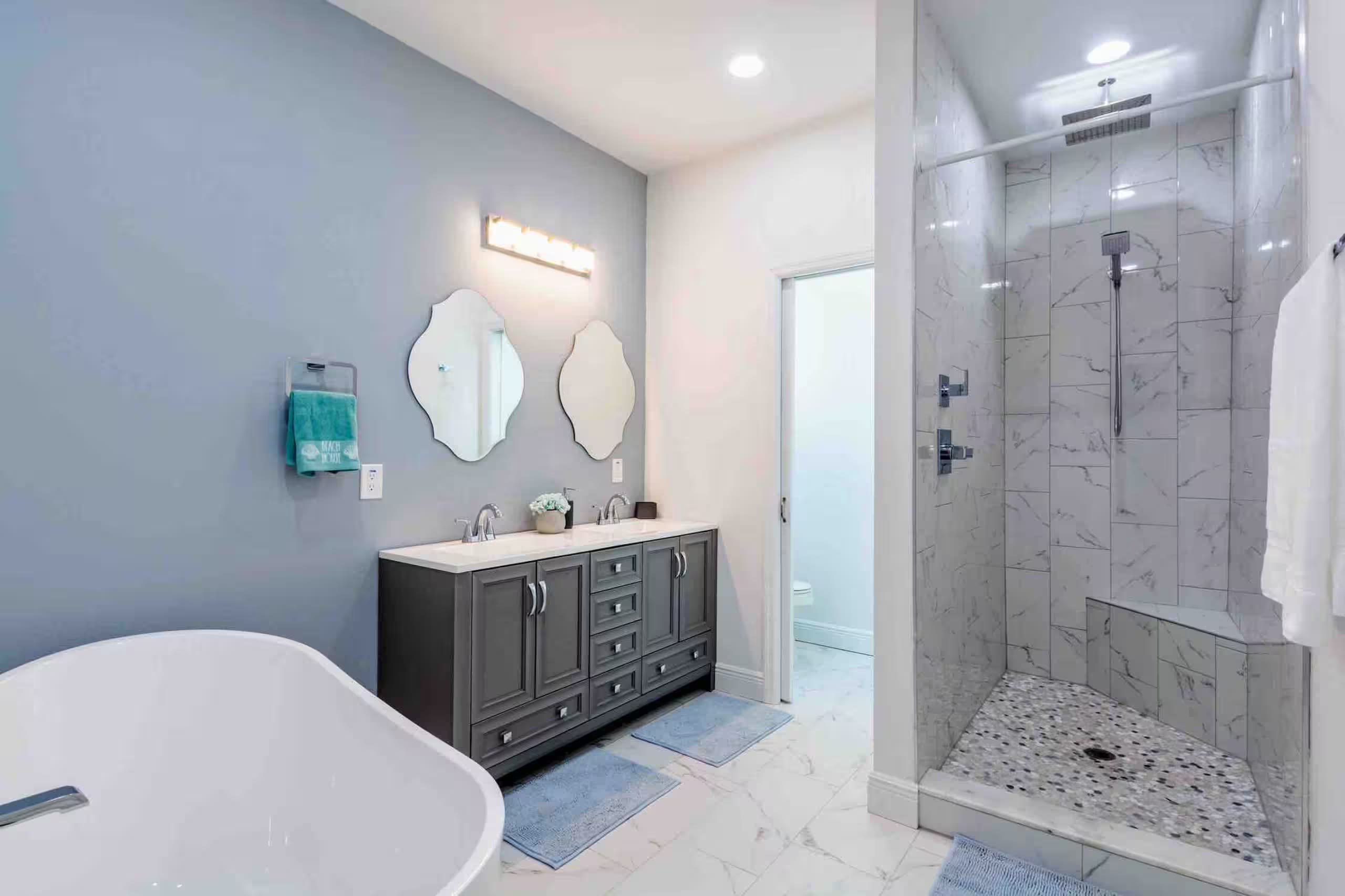 Primary bathroom with a freestanding soaking tub, dual-mirror vanity, and a separate marble-tiled walk-in shower