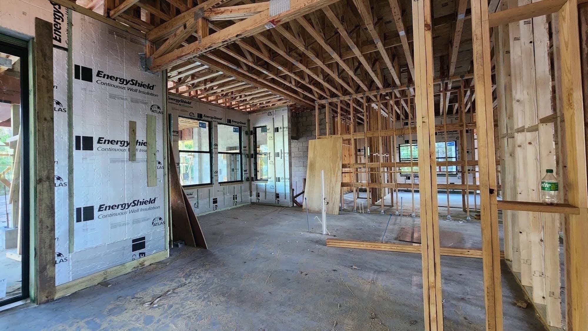 Framed interior room with EnergyShield continuous wall insulation panels installed on the concrete block walls, exposed roof framing overhead, and window openings looking out to the surrounding lot