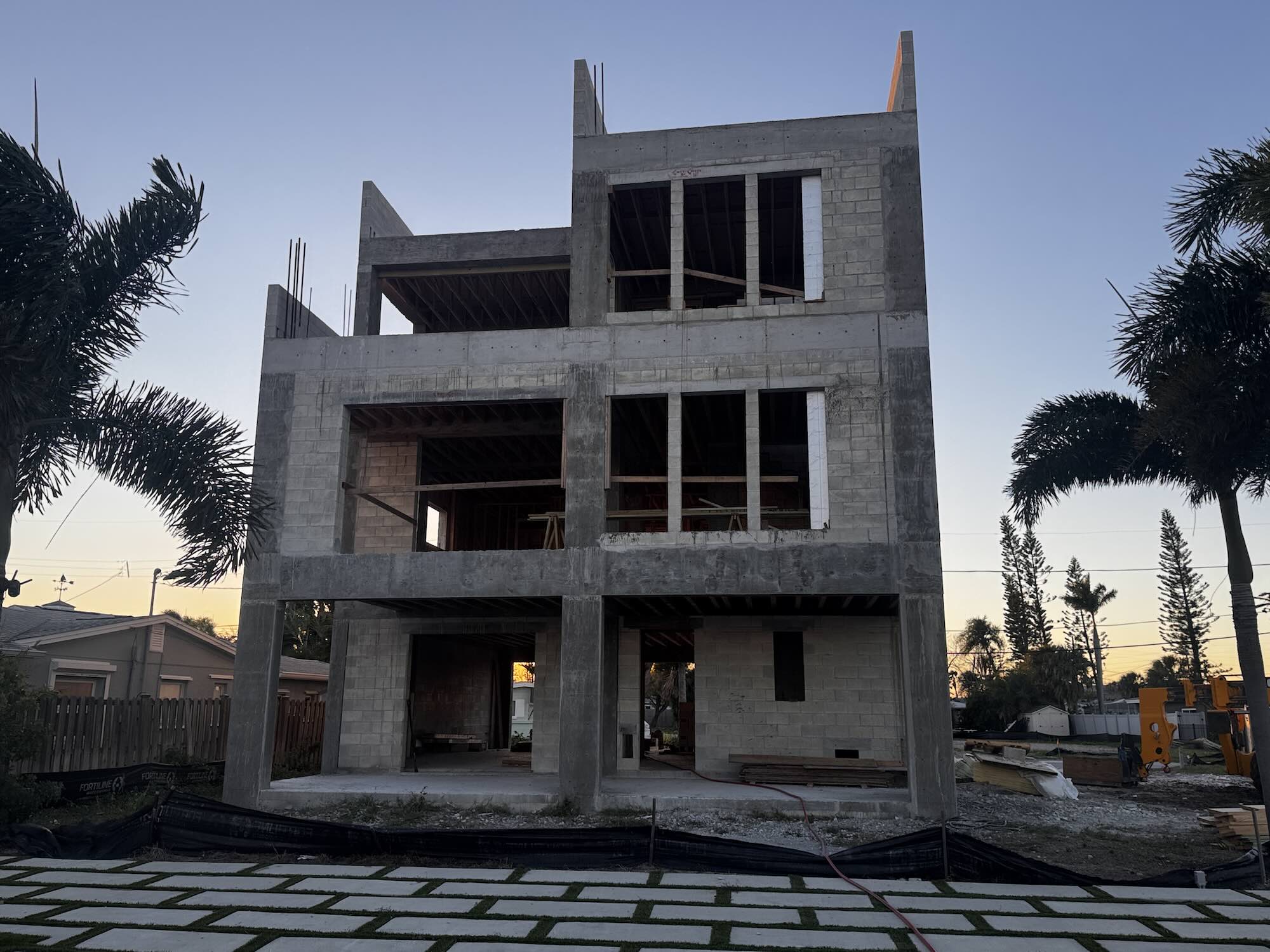 Three-story concrete block and tie-beam shell of a waterfront home at dusk