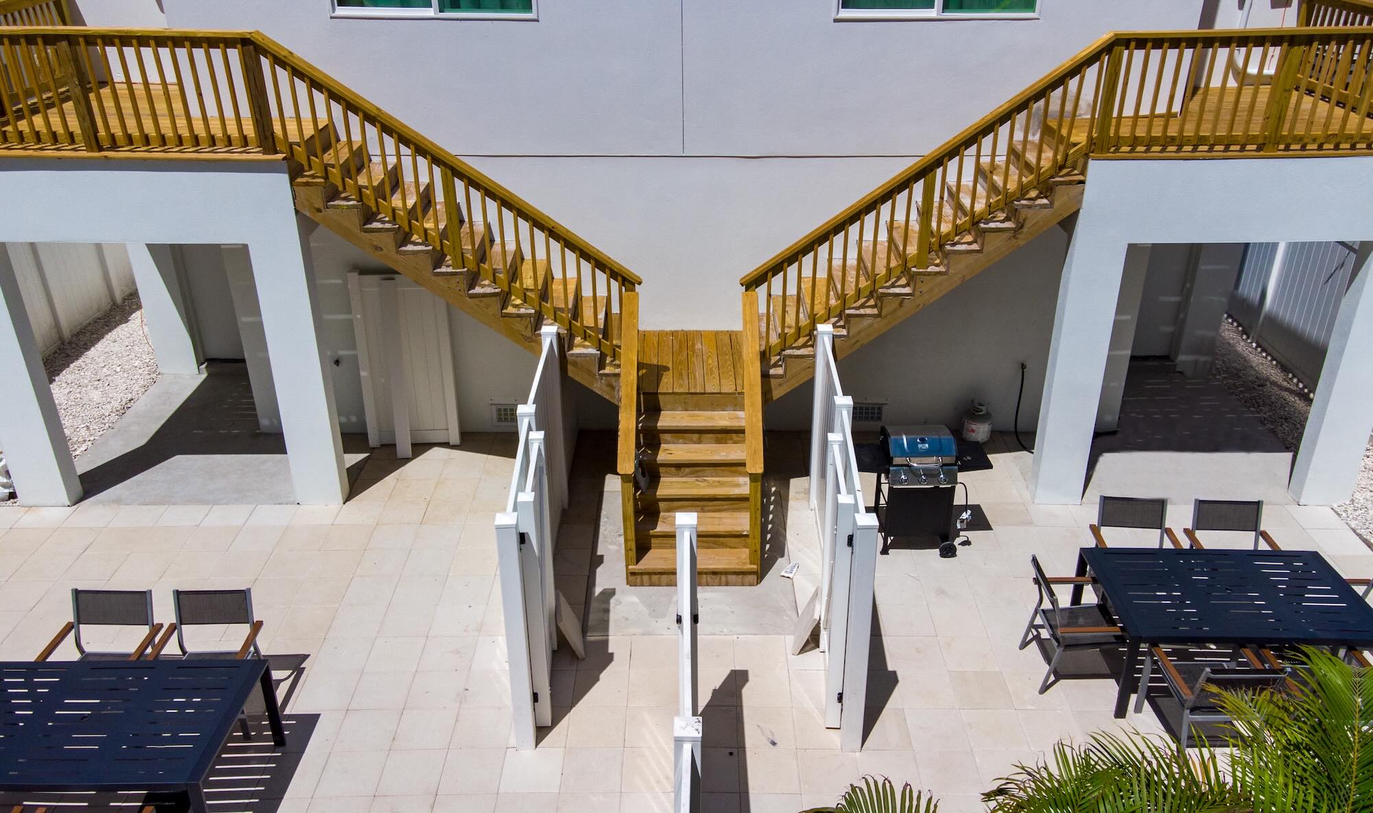 Aerial view of a shared exterior staircase connecting two mirrored units, with a ground-floor patio and outdoor dining area between them