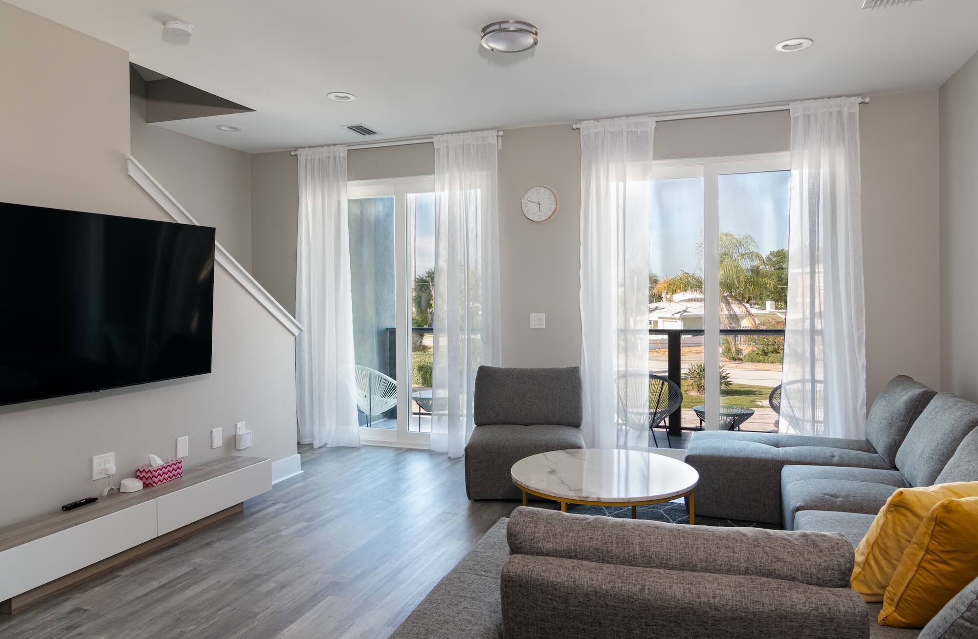Living room with a wall-mounted TV, gray sectional seating, and sliding doors opening to a water-view balcony