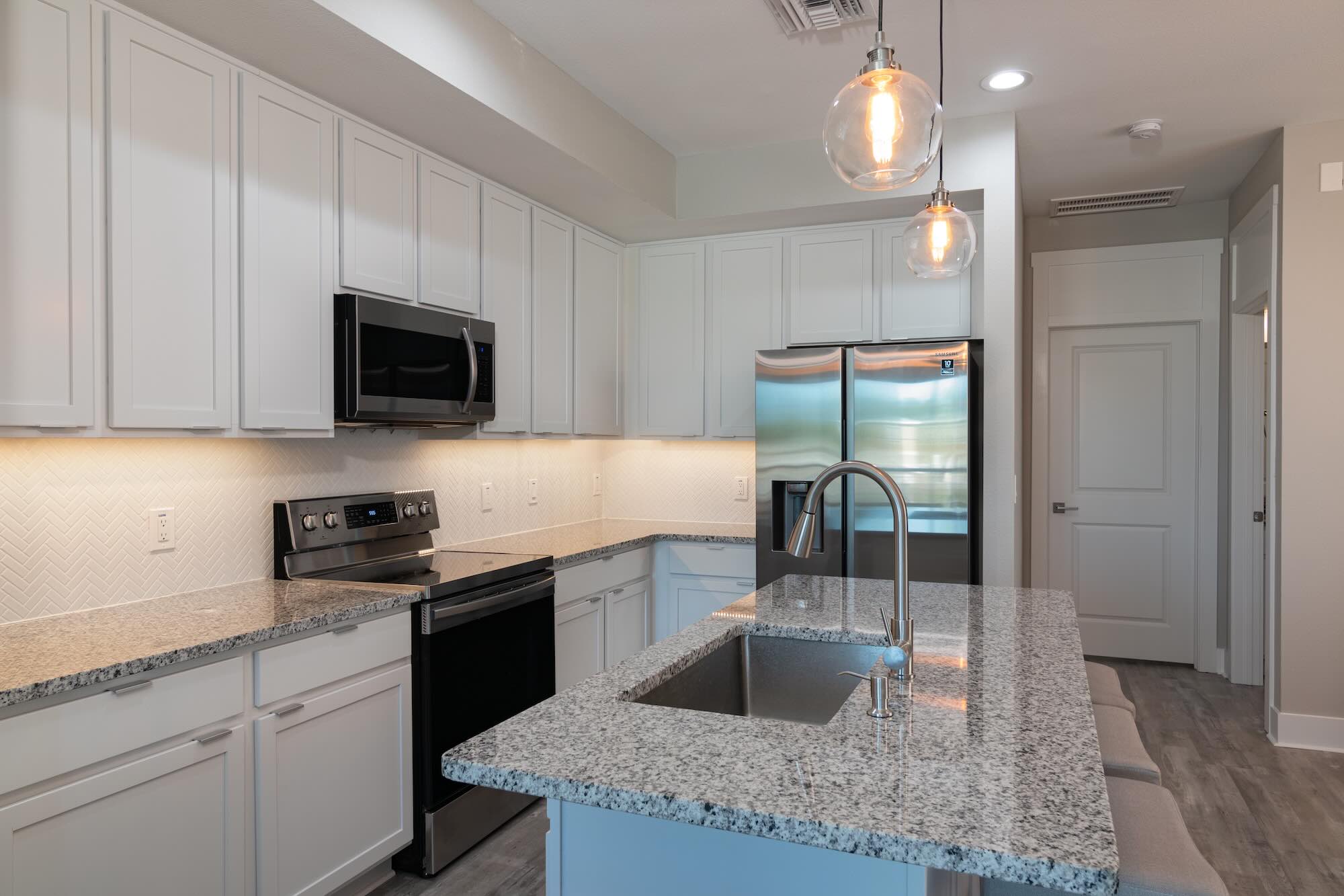 Kitchen with white cabinetry, granite countertops, a herringbone tile backsplash, and stainless steel appliances