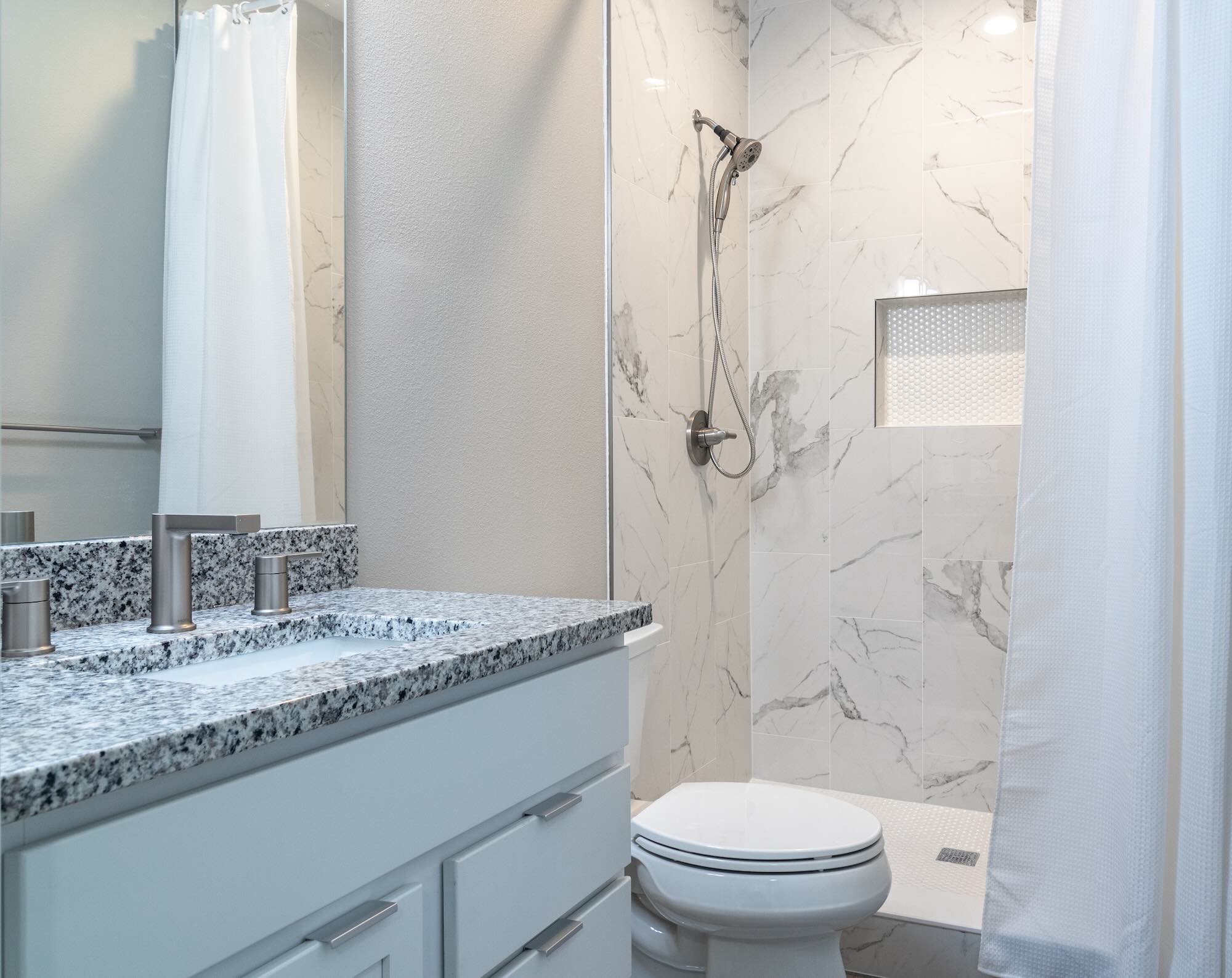 Bathroom with a granite vanity top, marble tile shower surround, and a built-in tile niche
