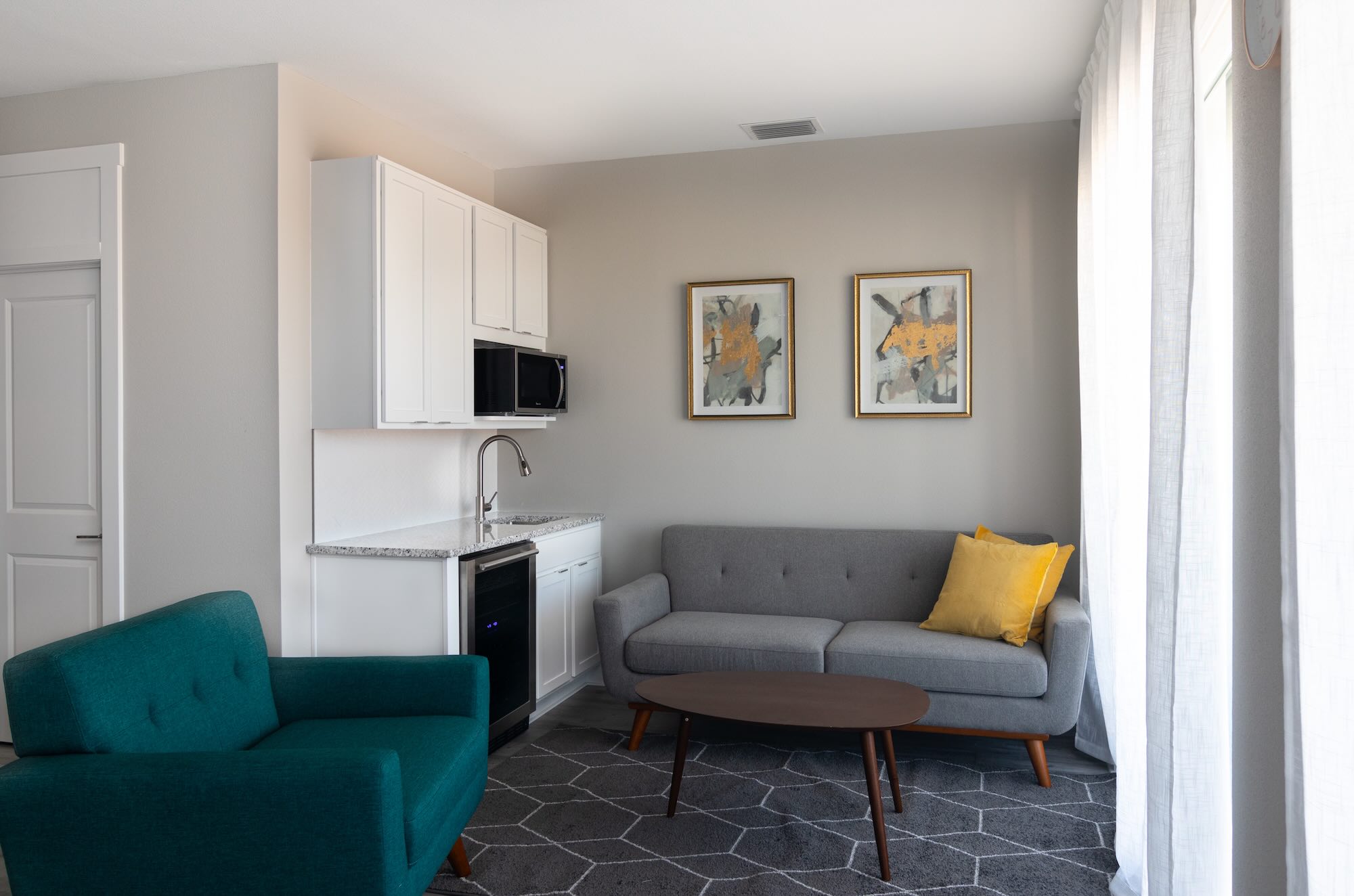 Upper-level loft lounge with a small kitchenette, teal accent chairs, and a gray sofa