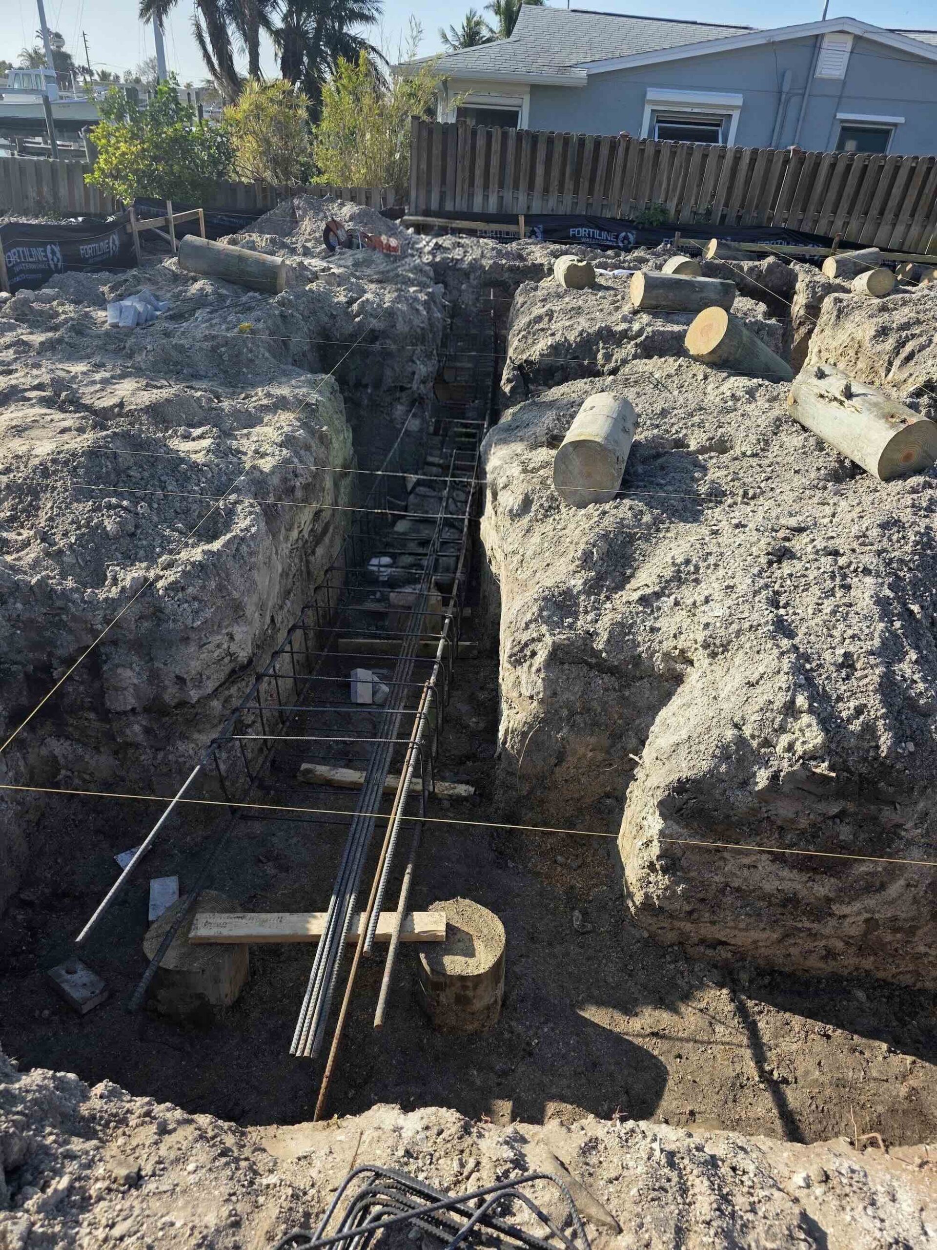 Excavated foundation trench with rebar cage for a waterfront home, canal visible in background