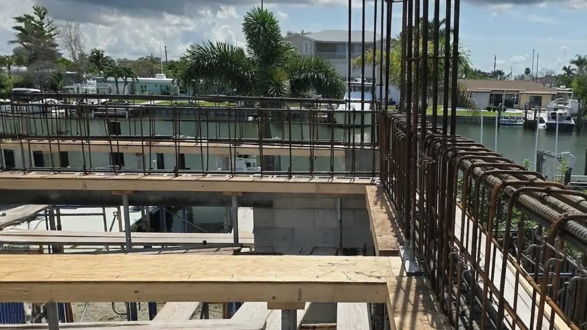Rebar cage running along the formed edge of an elevated concrete floor at a Madeira Beach waterfront lot, storm clouds visible over the canal