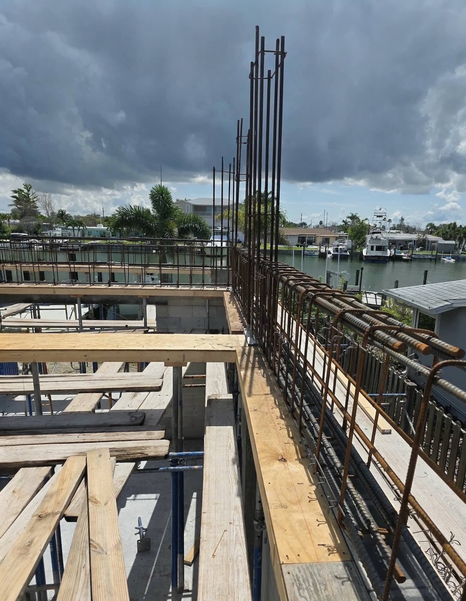 Rebar cage running along the formed edge of an elevated concrete floor at a Madeira Beach waterfront lot, storm clouds visible over the canal