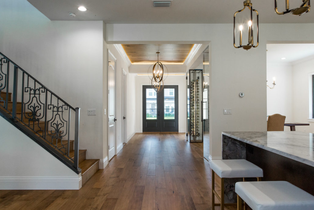 Entry hallway with wood flooring, a wrought-iron staircase railing, and a glass-enclosed wine wall visible ahead
