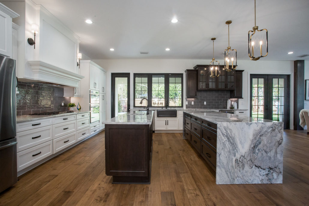 Kitchen with dark wood cabinetry, white perimeter cabinets, dual islands, and a stone waterfall-edge countertop
