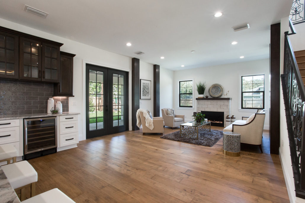 Living room with a stone fireplace, French doors to the backyard, and a wet bar with glass-front cabinetry