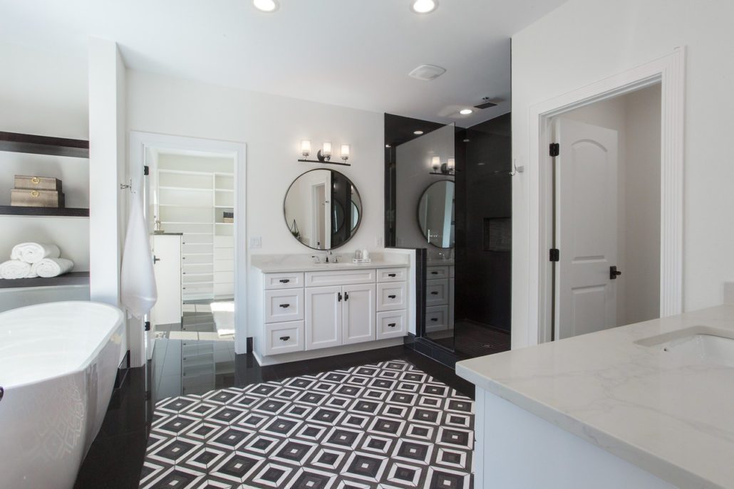Primary bathroom with a freestanding tub, dual vanity, black tile shower, and geometric black-and-white floor tile