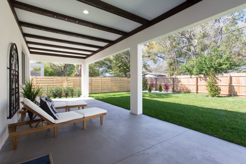 Covered rear patio with a wood-beamed ceiling, outdoor lounge seating, and a wood privacy fence