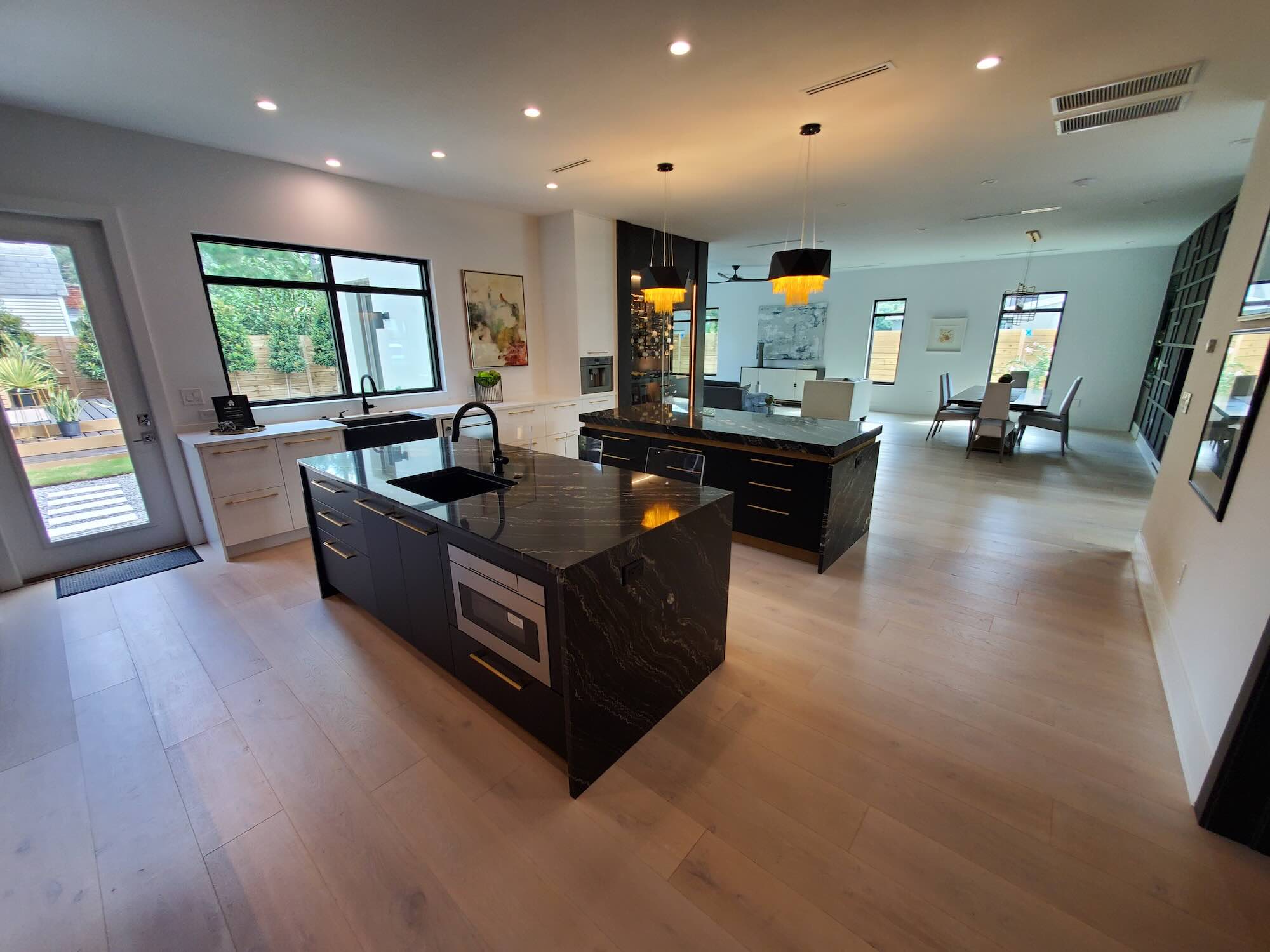 Kitchen with two black-and-gold stone waterfall islands, pendant lighting, and an open view into the dining and living areas