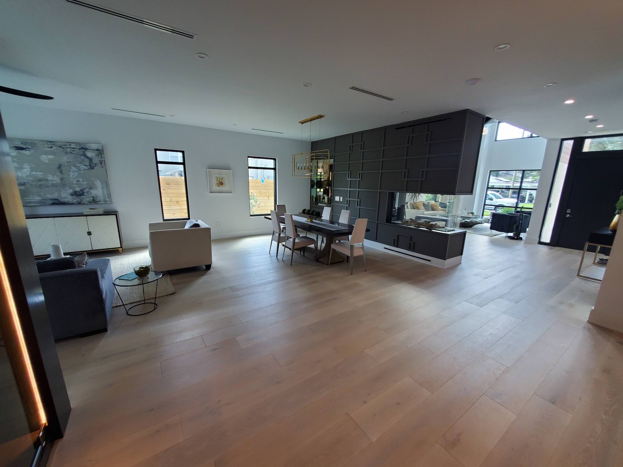 Open living and dining room with a gray geometric-paneled accent wall, a suspended fireplace box, and a linear chandelier over the dining table