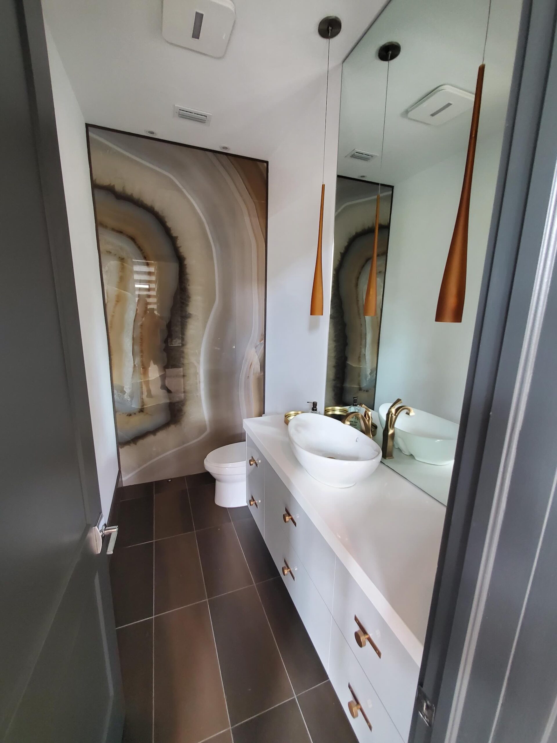 Powder bathroom with a book-matched agate stone feature wall, a white vessel sink, gold fixtures, and a copper pendant light