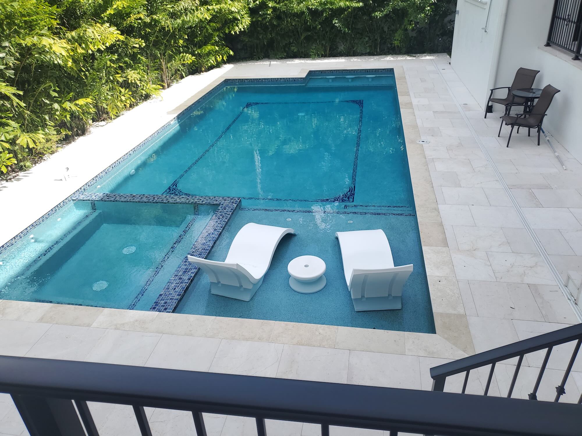 Rectangular pool with a tanning ledge, tile accents, and floating lounge chairs, bordered by stone decking