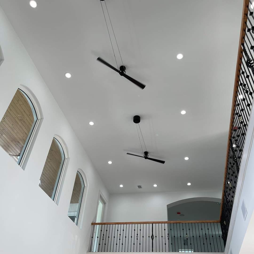 Double-height stairwell with arched windows, wrought-iron railing, and paddle ceiling fans