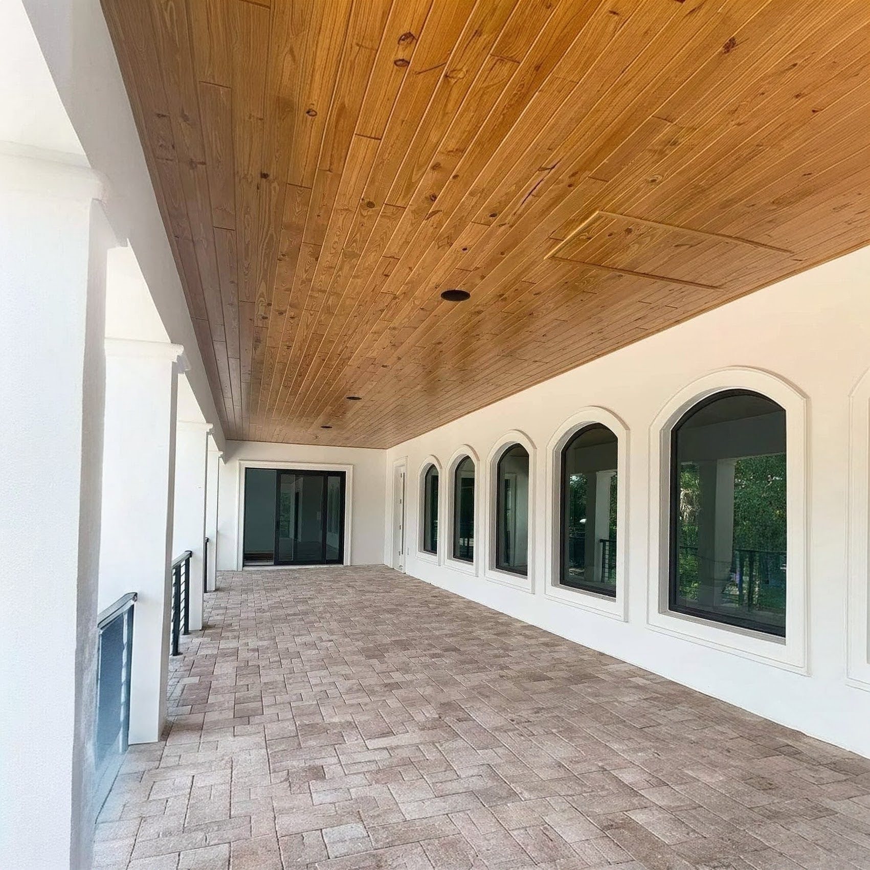 Covered upper loggia with a wood plank ceiling and a row of arched windows along the wall