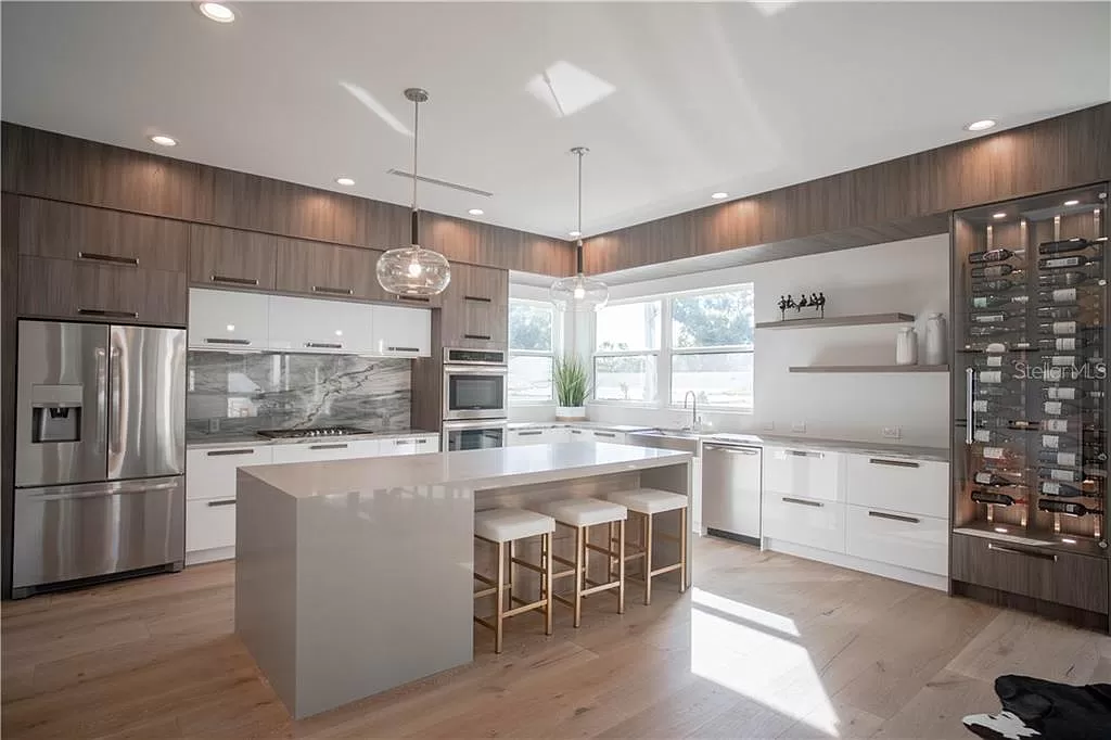 Open kitchen and dining area with a dark wood dining table set for entertaining, glossy white cabinetry, and pendant lighting over a central island