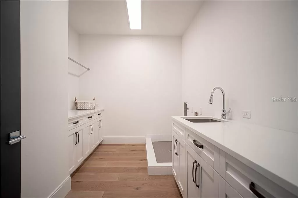 Laundry room with white shaker cabinetry, a built-in dog wash station with a step-up tiled basin, and a farmhouse sink