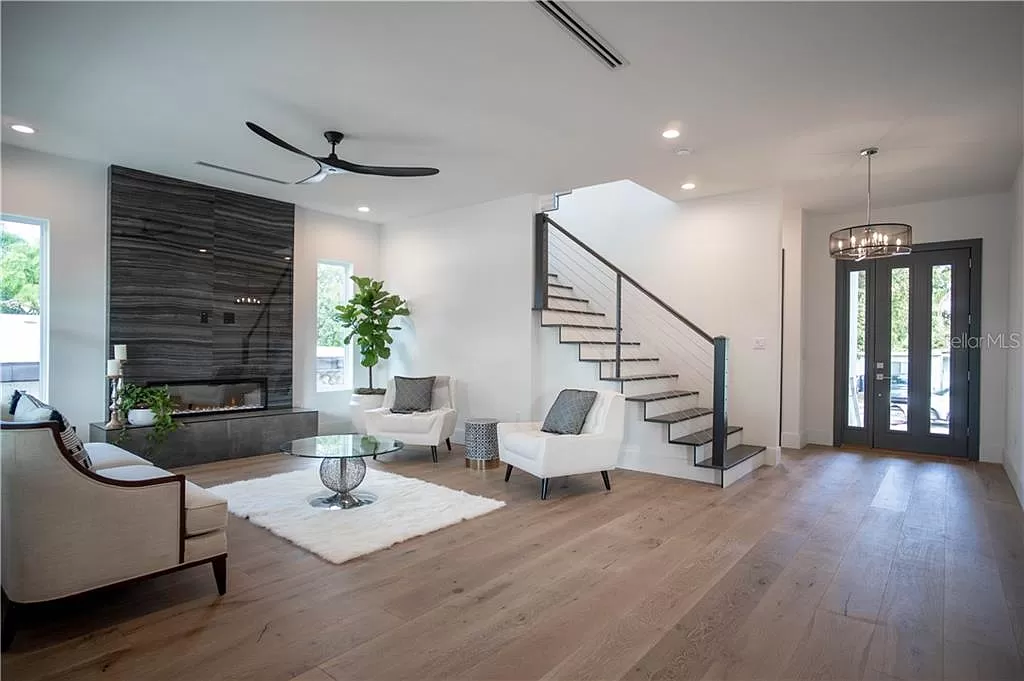 Open living room and entry with a black steel open-riser staircase, a linear gas fireplace with dark stone surround, and white oak flooring
