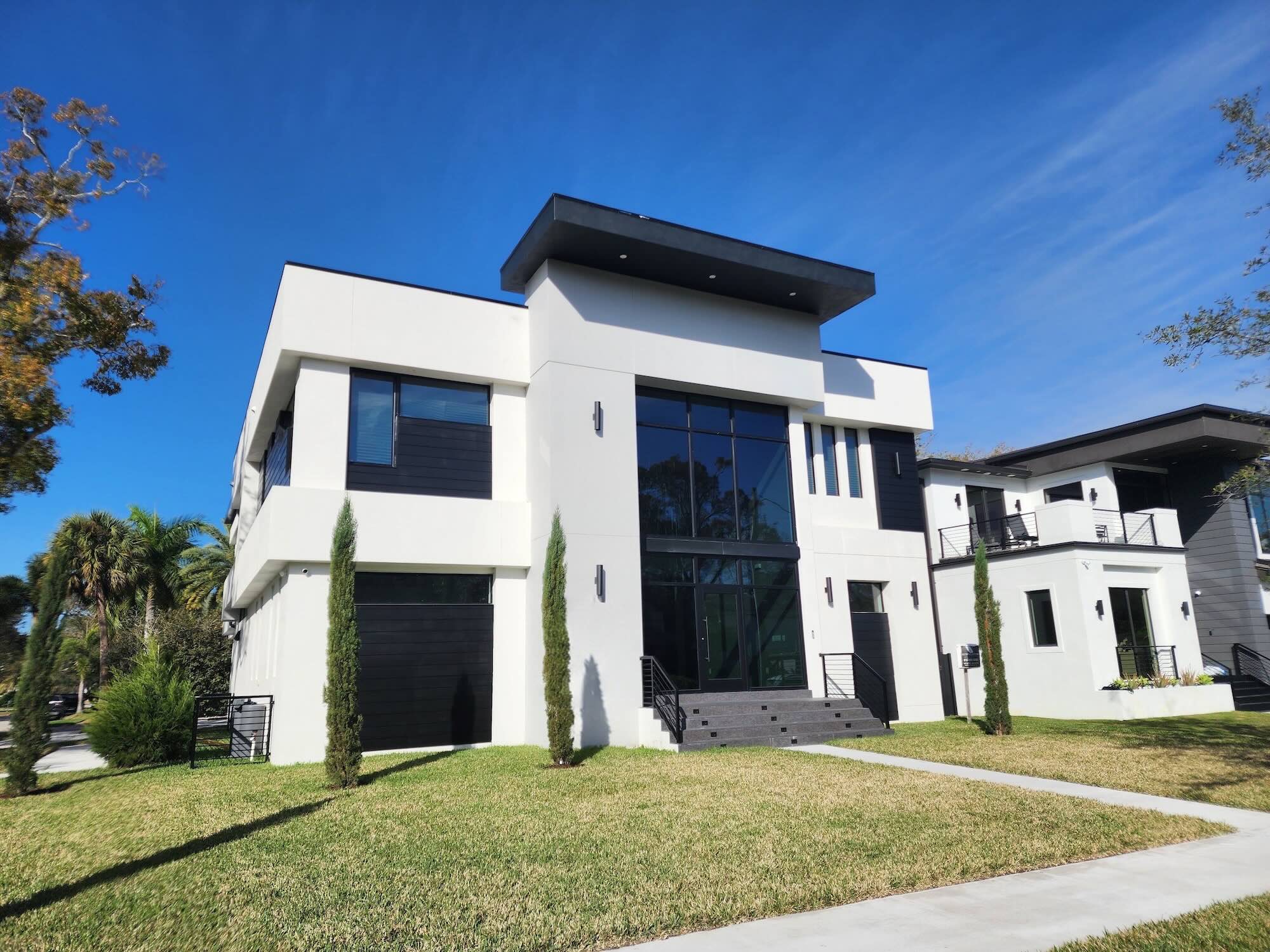 Angled exterior view of a modern South Tampa home showing multi-level rooflines and black window bands under mature oak trees