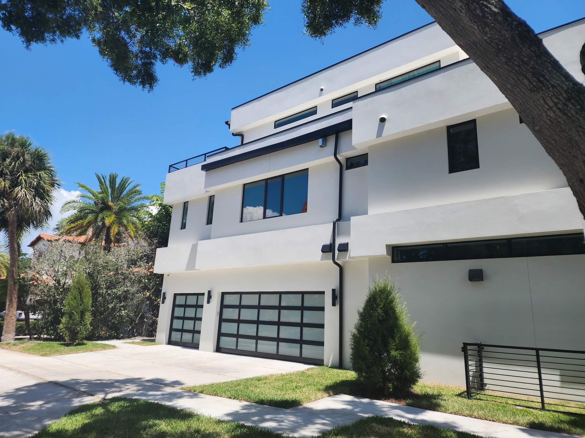 Side exterior view of a modern home showing a two-car garage with dark paneled doors and white stucco walls