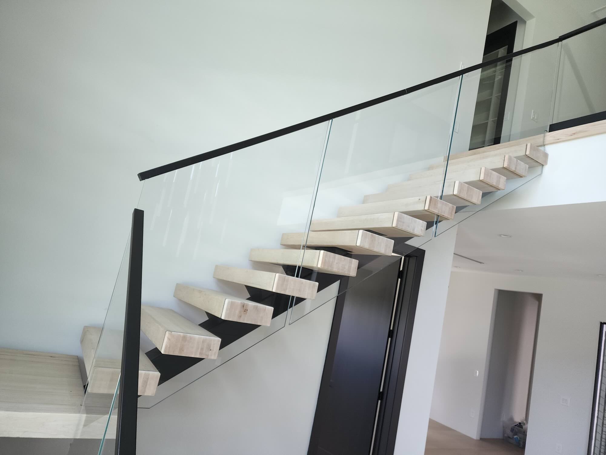 Open-riser wood staircase with a black steel frame and full-height glass railing inside a modern home