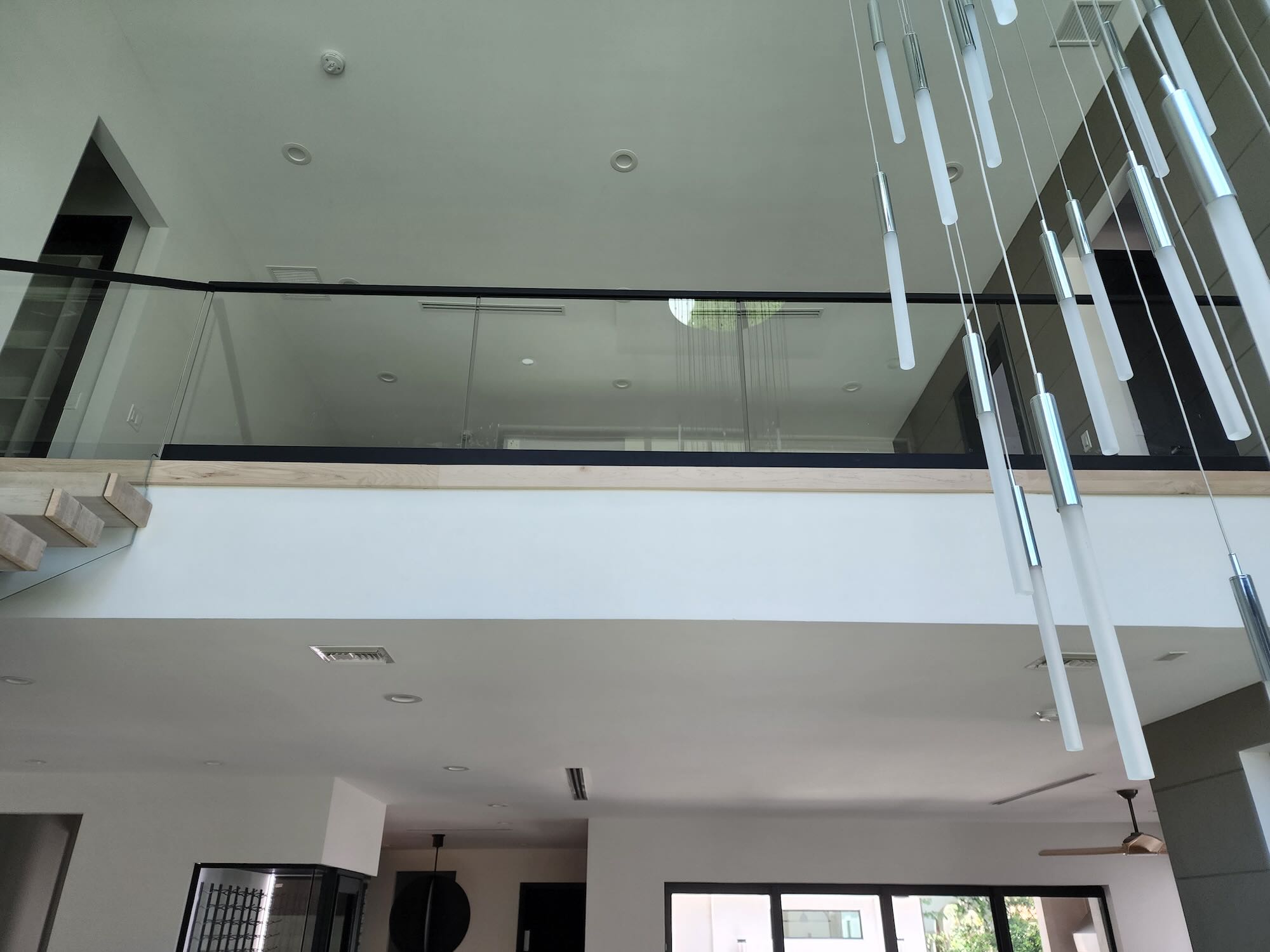 Double-height living space with a multi-pendant linear light fixture and a glass-railed loft overlook