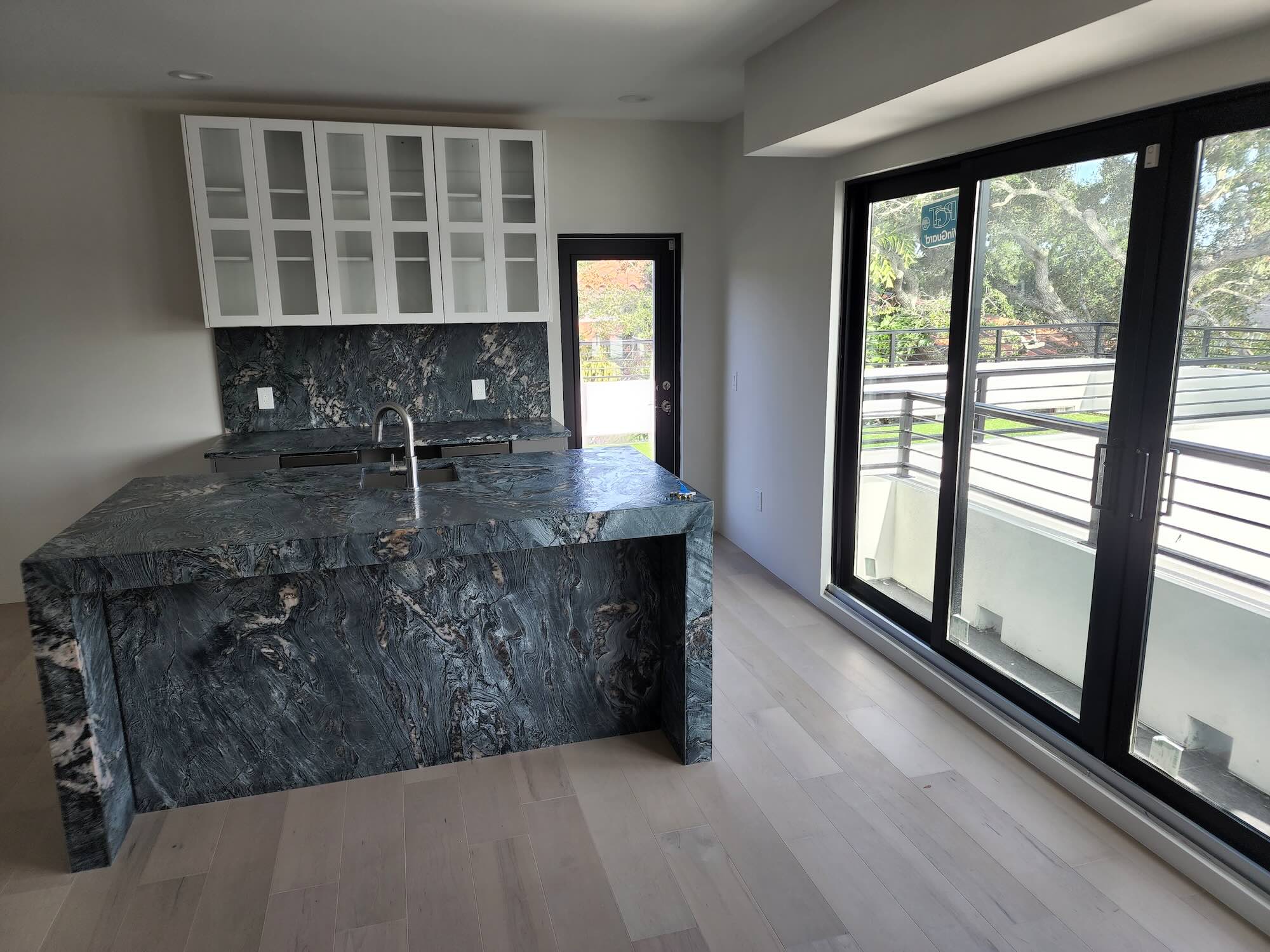 Waterfall-edge stone kitchen island with dark veined stone and glass-front upper cabinets