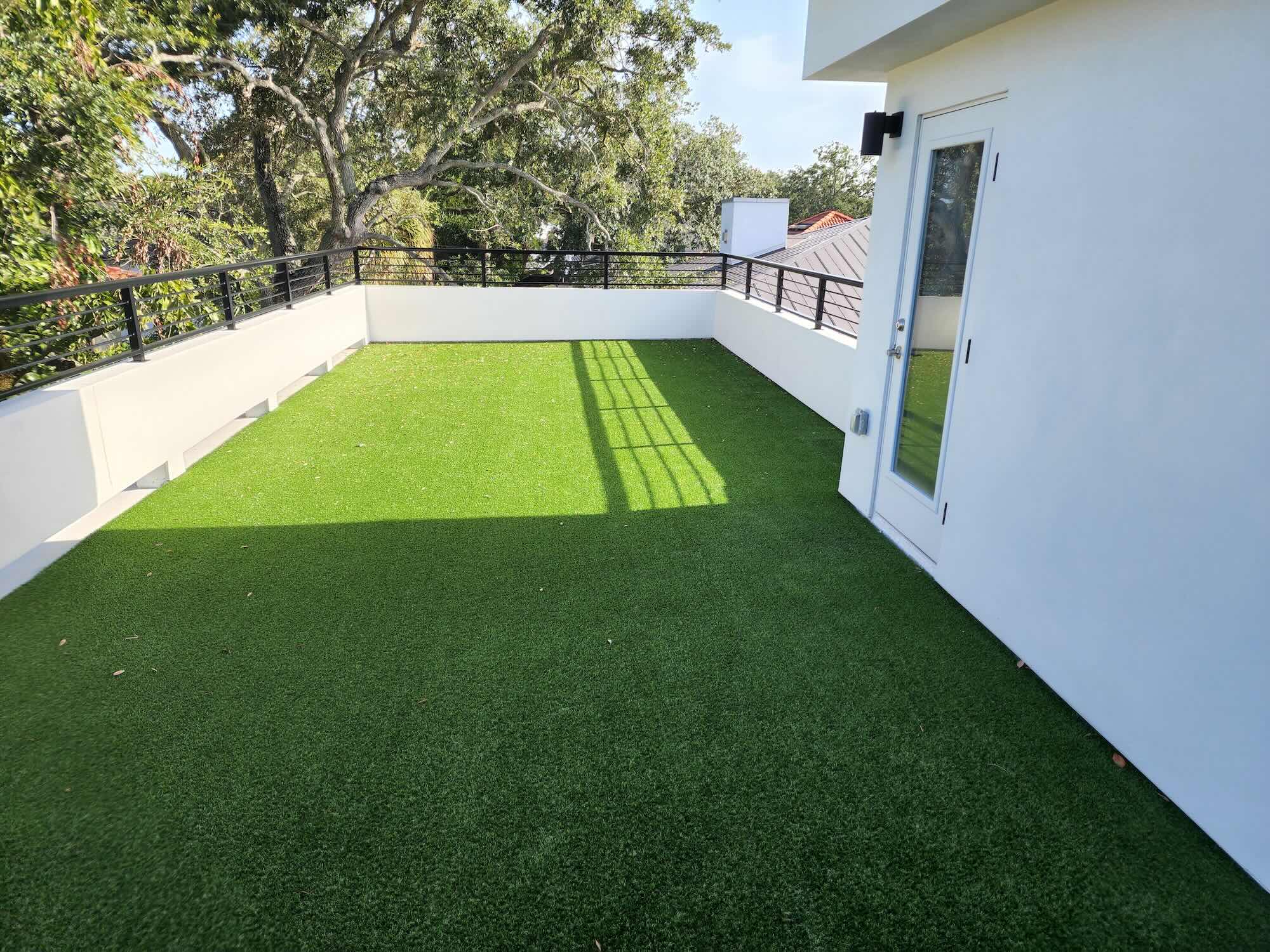 Rooftop terrace with artificial turf and black metal railing, surrounded by tree canopy