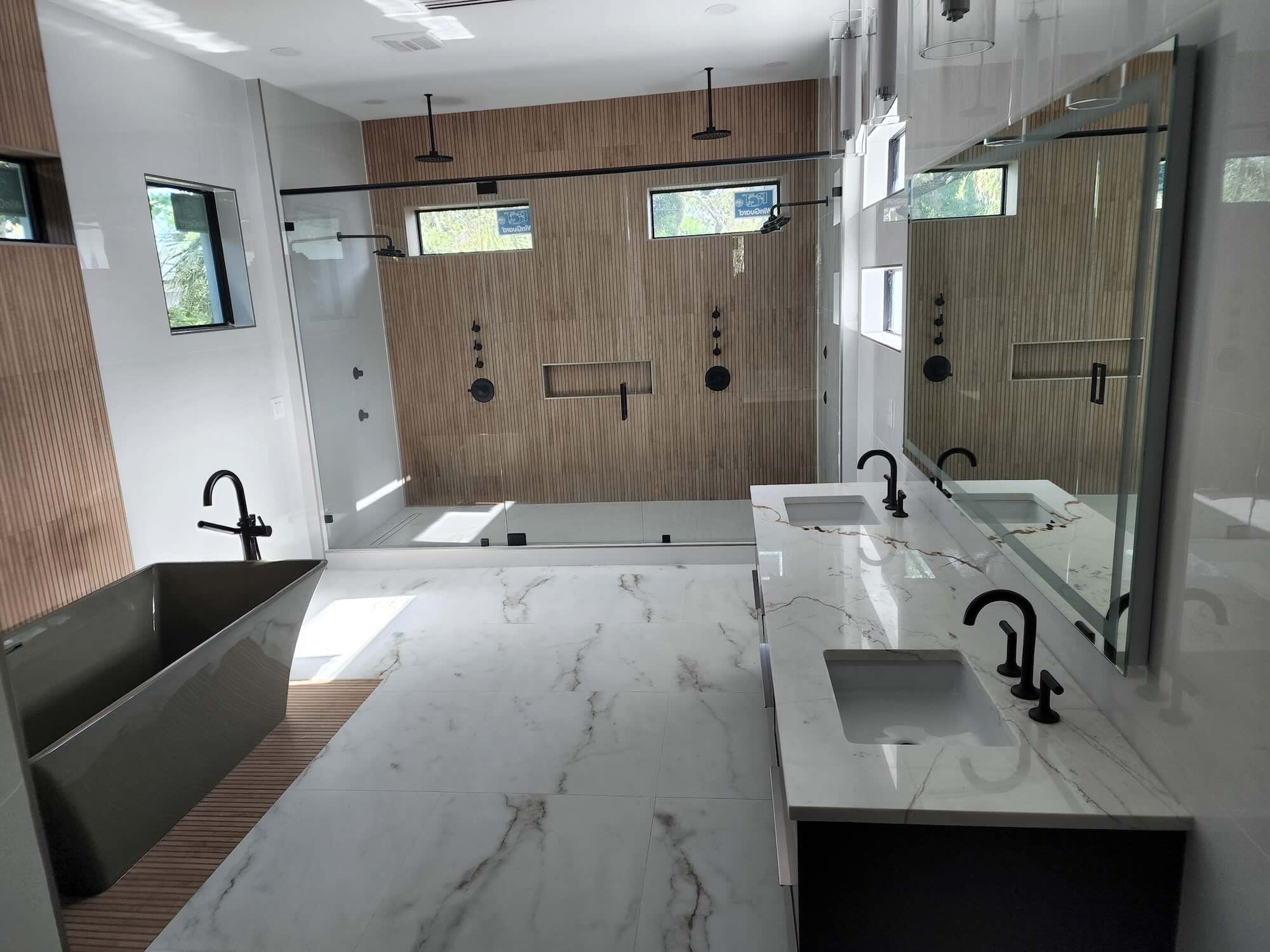 Primary bathroom with dual vanity, marble flooring, wood-slat accent wall, and a glass-enclosed shower with dual rain heads