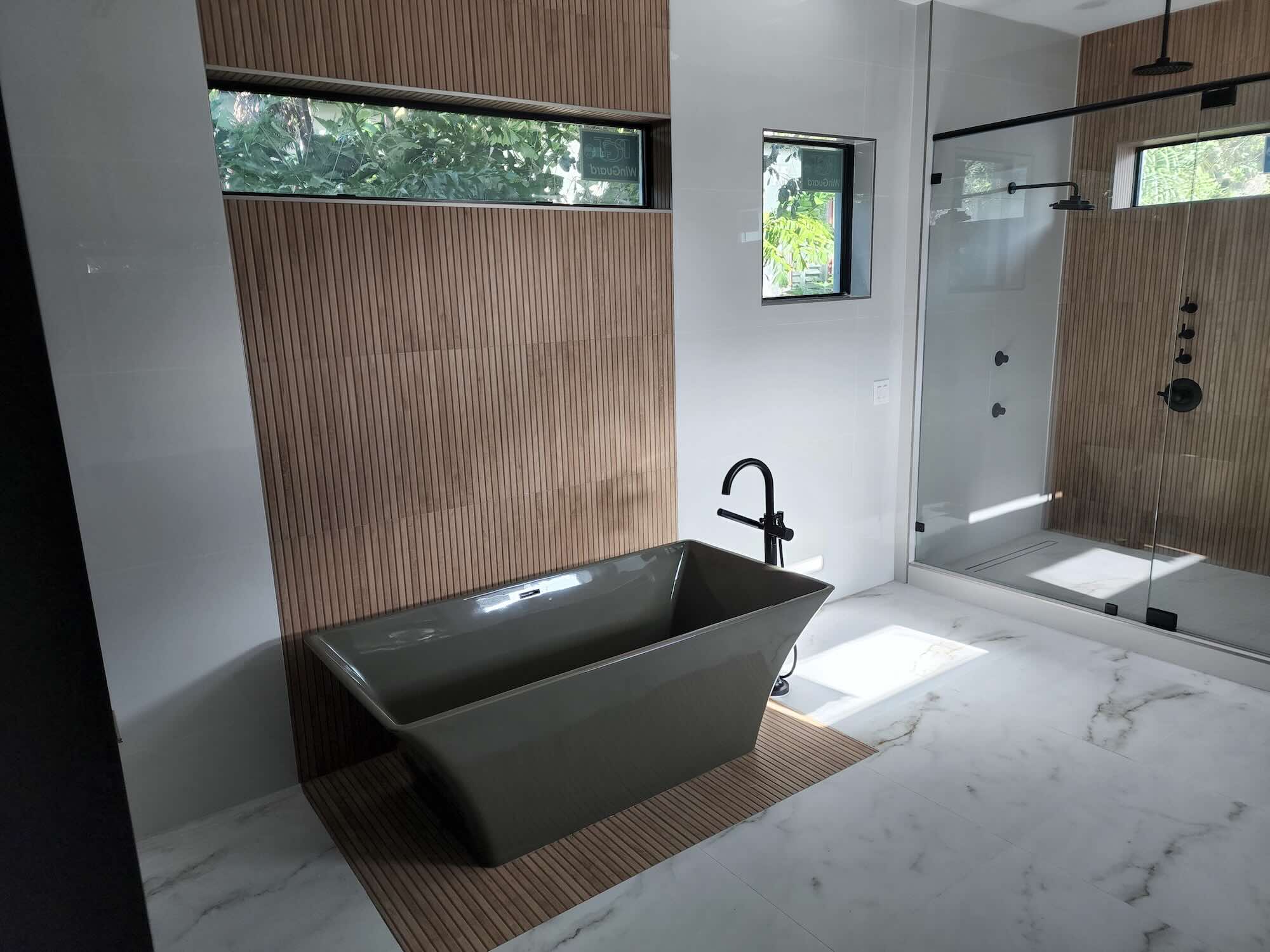 Freestanding vessel-style bathtub against a wood-slat accent wall with a floor-mounted matte black tub filler