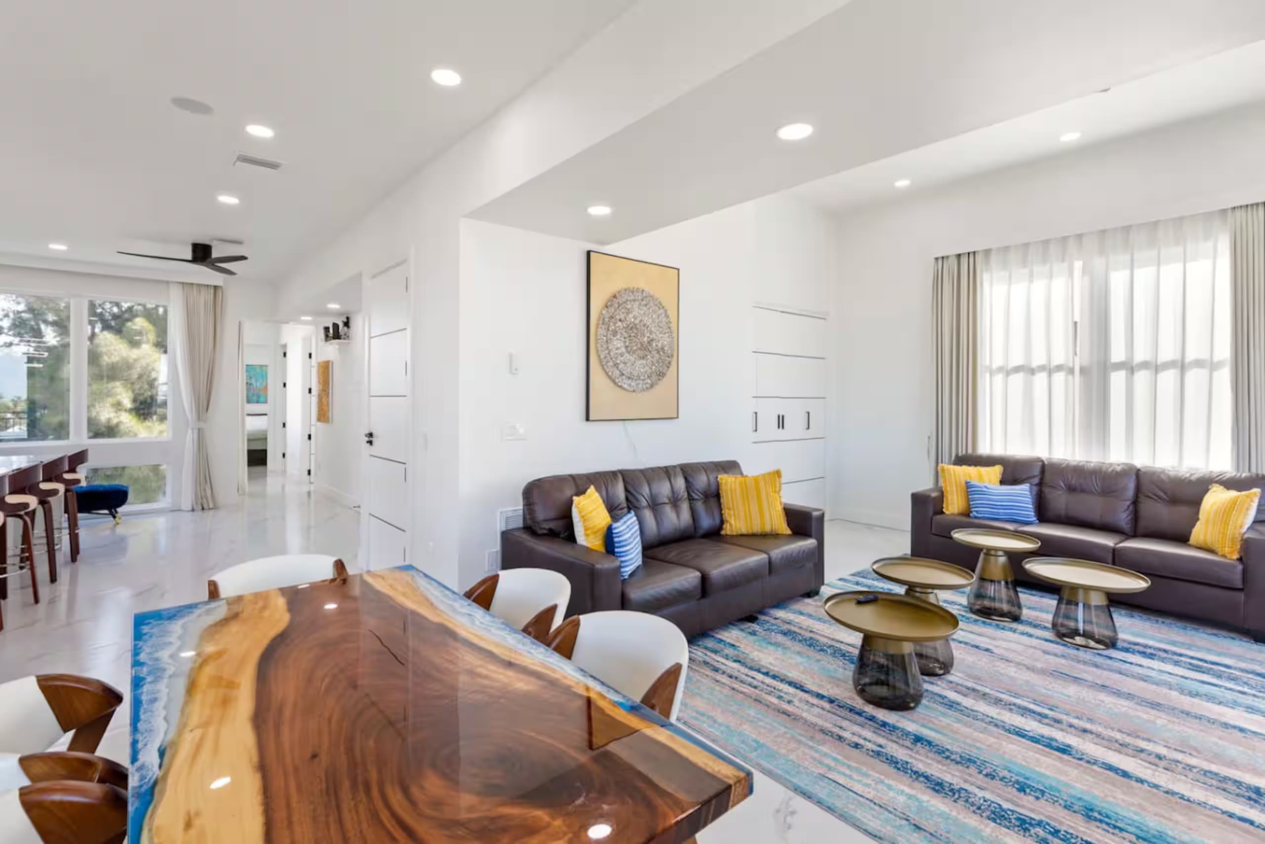Open living and dining area with a live-edge blue-resin wood dining table, leather sofas, and a patterned area rug