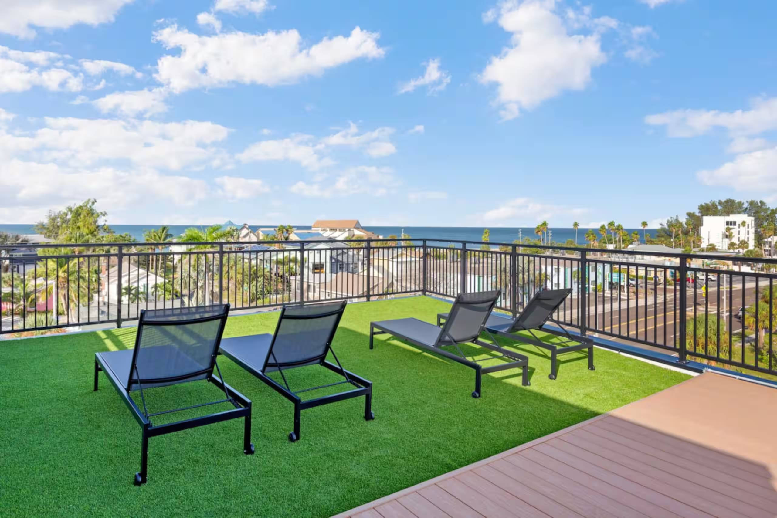 Rooftop deck with artificial turf, black lounge chairs, and an open view of the Gulf of Mexico over the railing