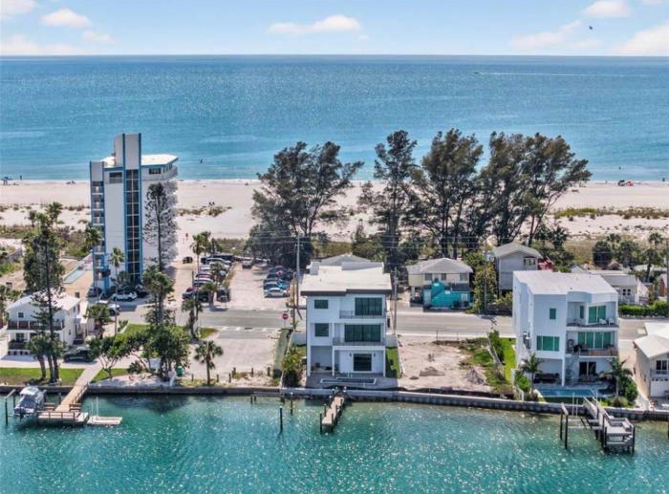 Aerial view of a three-story white home on the intracoastal waterway, steps from the beach, with a private dock