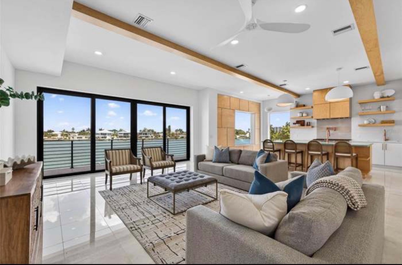 Living room with a sectional sofa, wood ceiling beams, and floor-to-ceiling sliding doors overlooking the water
