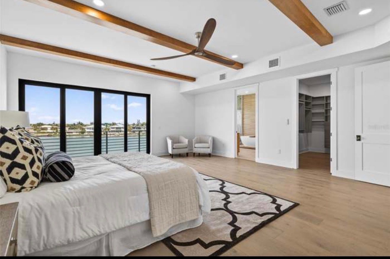 Primary bedroom with wood ceiling beams, hardwood floors, and a wall of glass doors facing the water