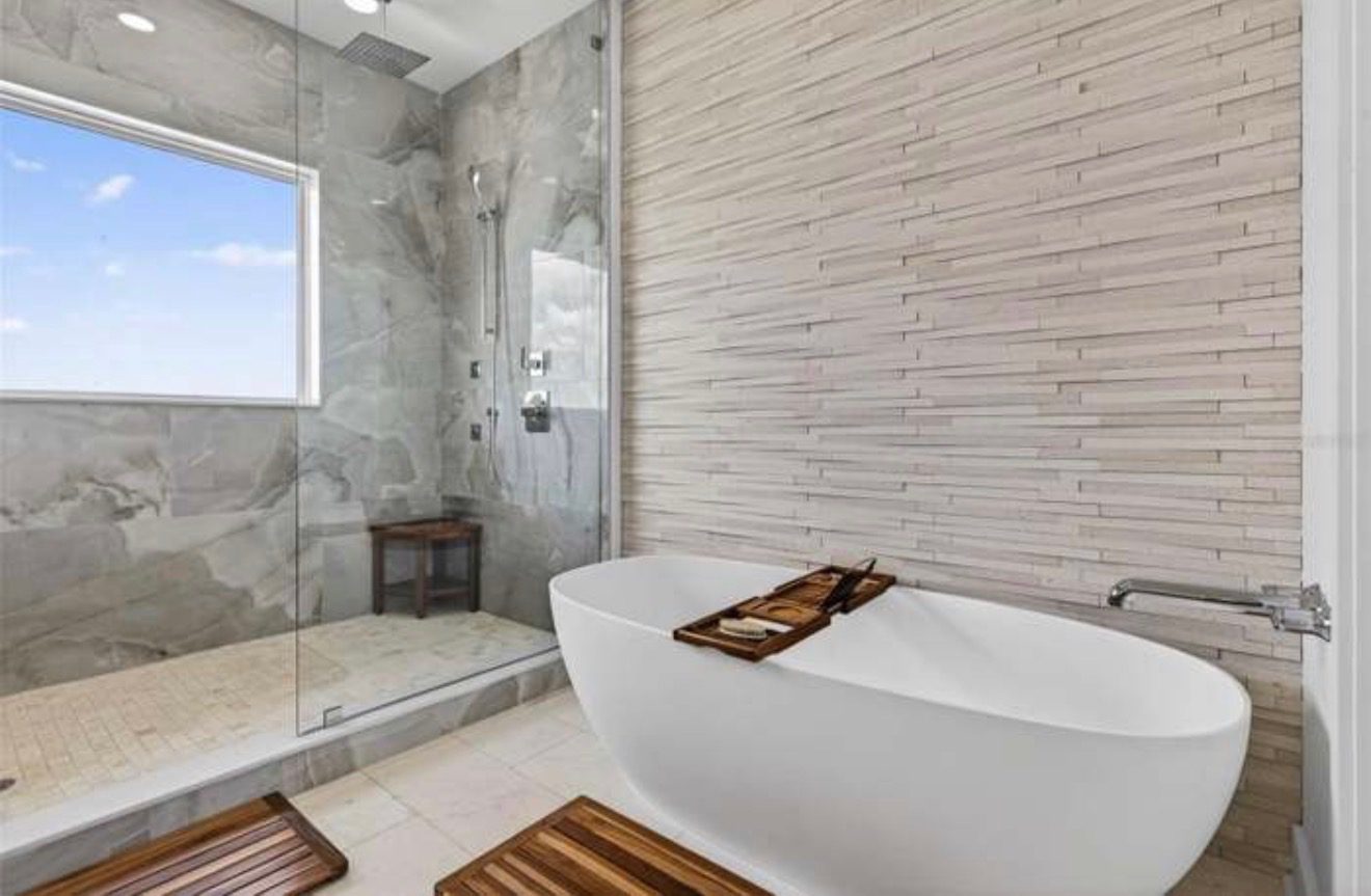 Primary bathroom with a freestanding tub, textured stone accent wall, and a glass-enclosed dual rain-head shower
