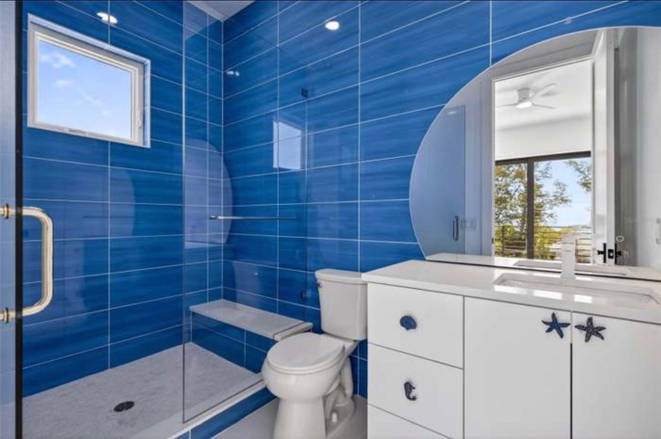 Guest bathroom with vivid blue tile, a glass shower enclosure, and coastal-themed cabinet hardware shaped like starfish and shells