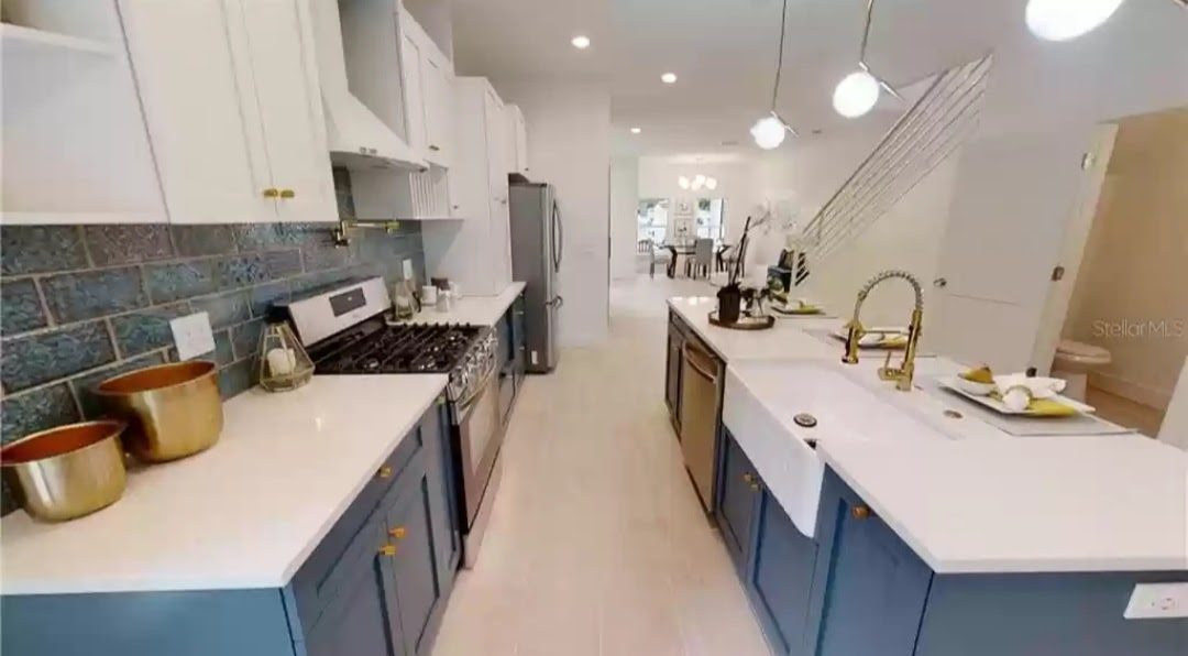 Galley kitchen with navy lower cabinets, white upper cabinets, brass hardware, and blue tile backsplash