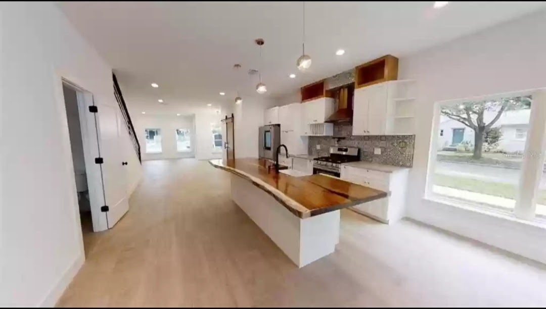 Kitchen with white cabinetry, live-edge wood island, and stainless steel refrigerator