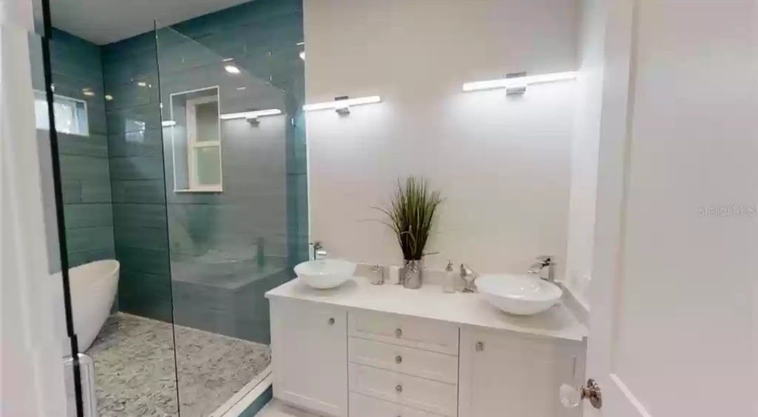 Primary bathroom with teal glass tile shower, freestanding tub, and dual vessel sink vanity